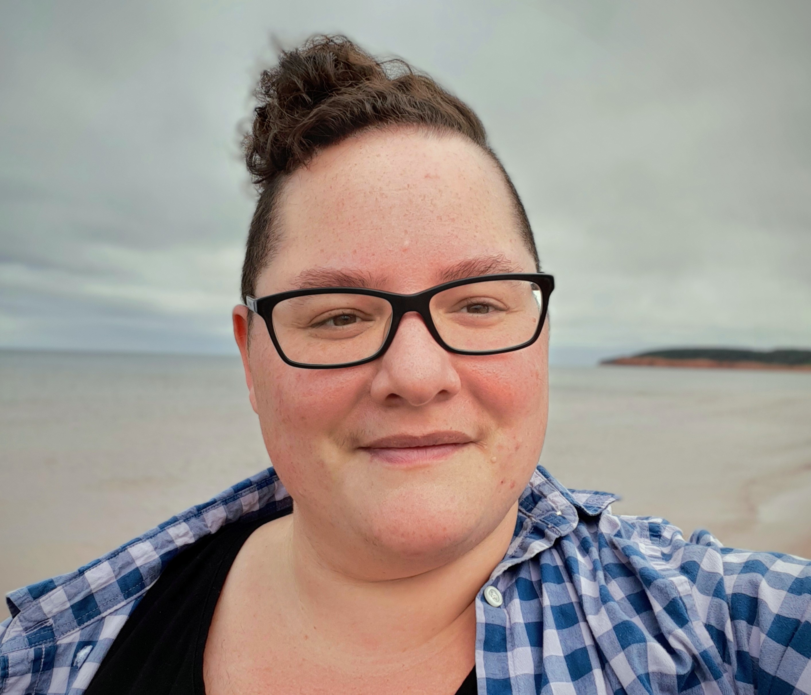 Headshot of androgynous light-skinned person wearing glasses on a beach